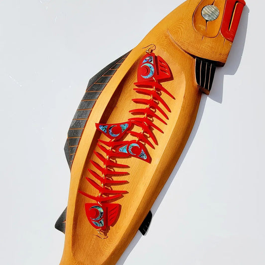 Copper Canoe Woman large red salmon ghost earrings in red acrylic laying inside a carved wooden fish bowl.