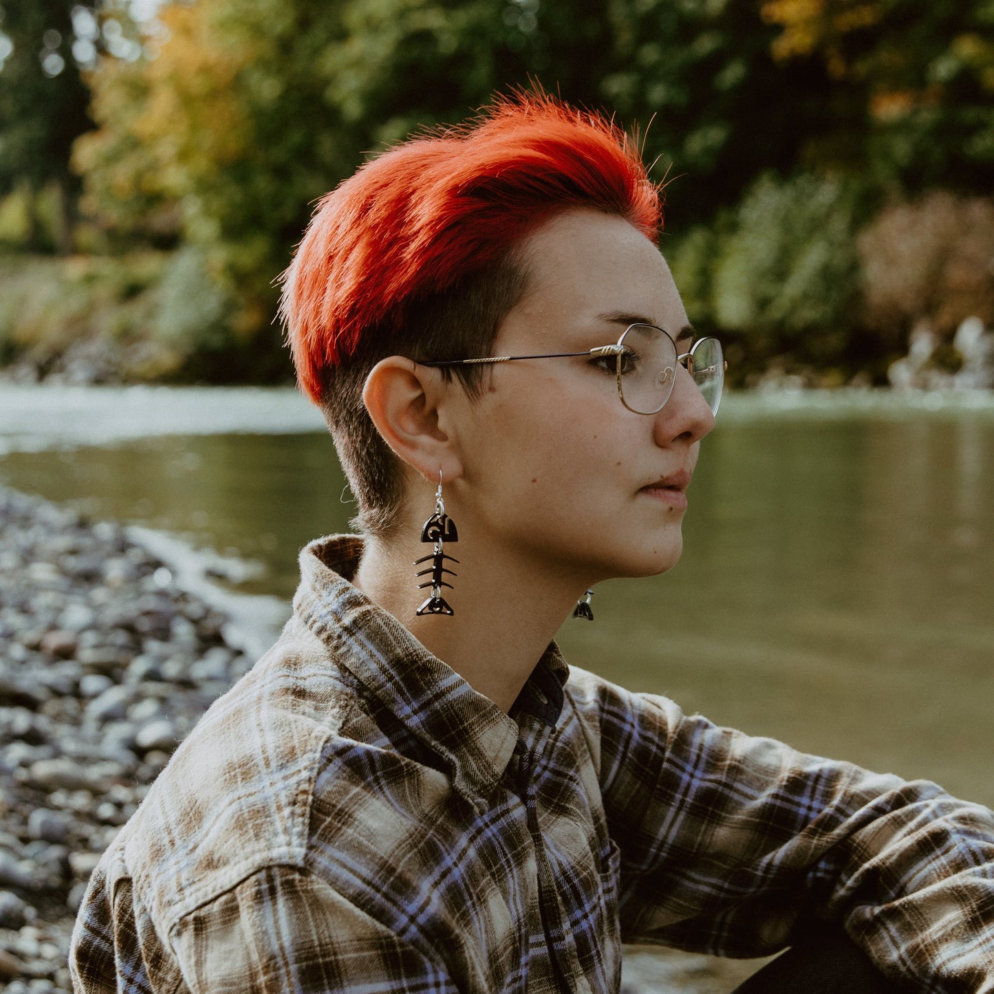 Person with red hair and Salmon Ghost (Small) earrings by a river.