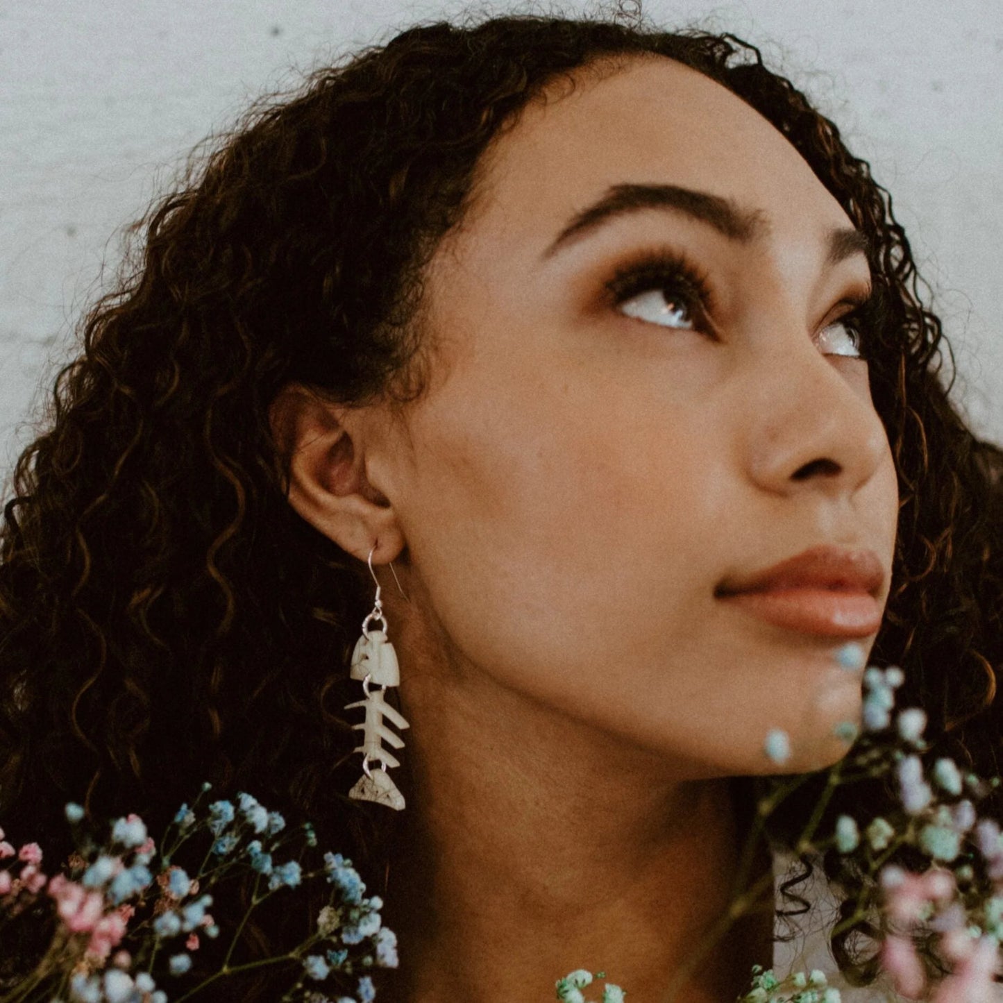 A woman looking upward showcases the ivory acrylic small salmon ghost earring from Copper Canoe Woman.