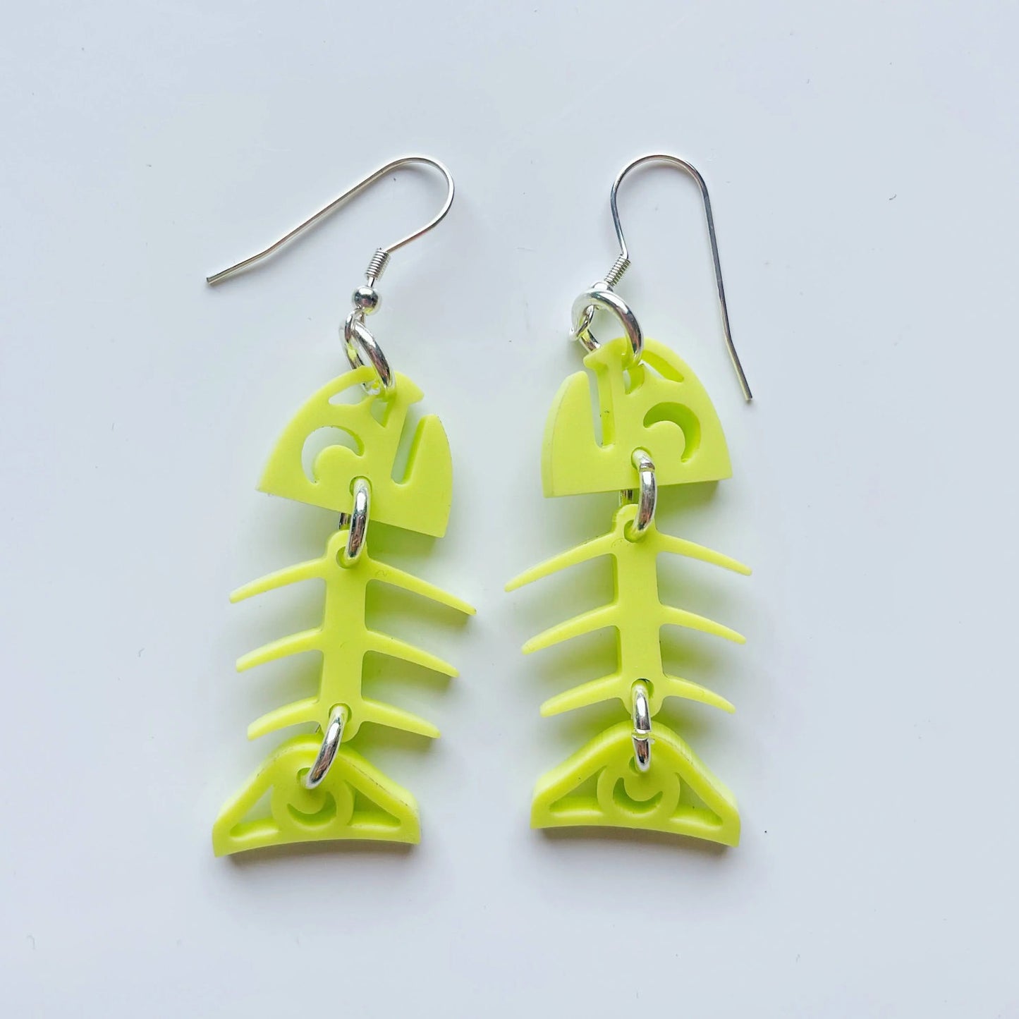 A pair of neon pear acrylic small salmon ghost earrings from Copper Canoe Woman laying on a white background.