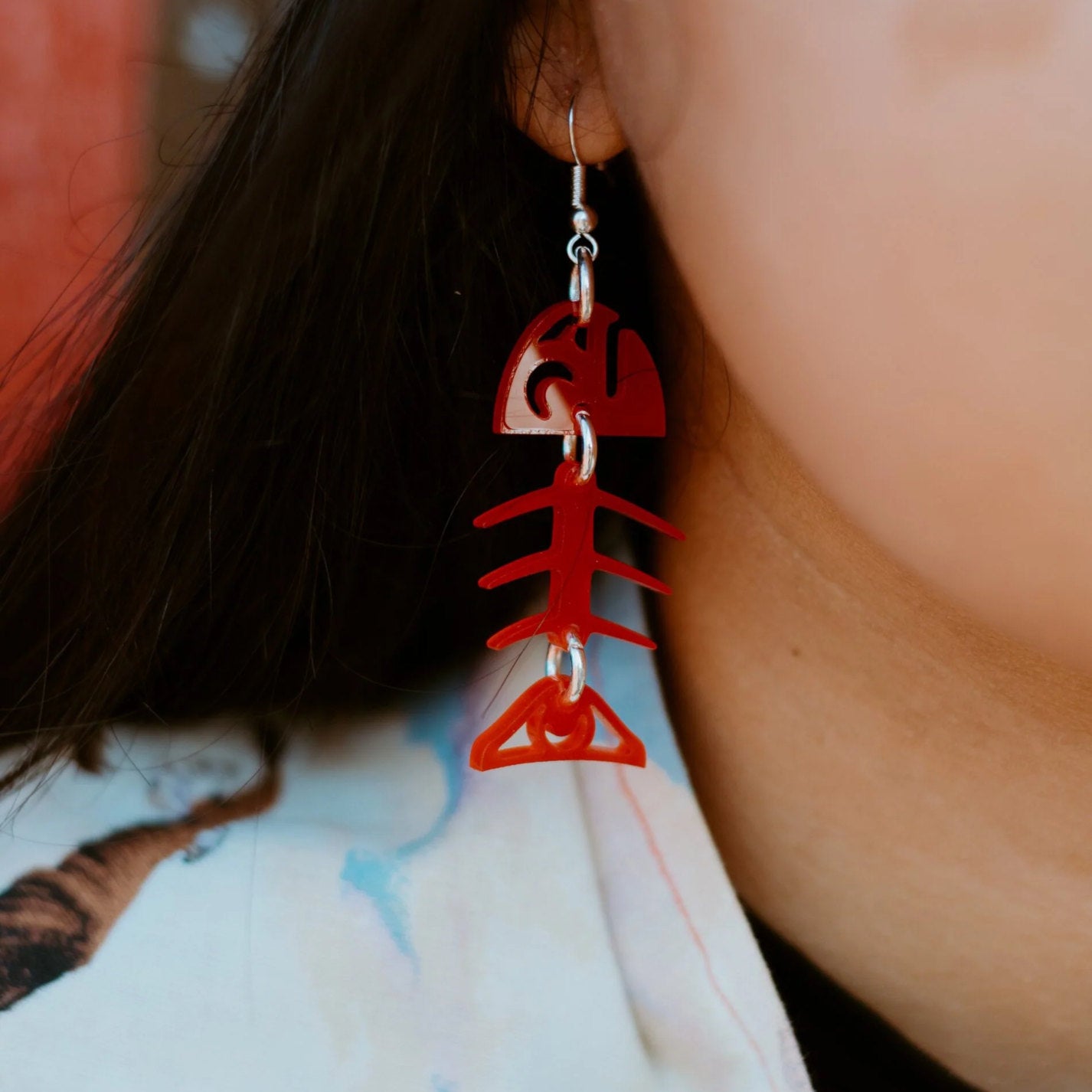 A close up of a model wearing the red acrylic small salmon ghost earring from Copper Canoe Woman.
