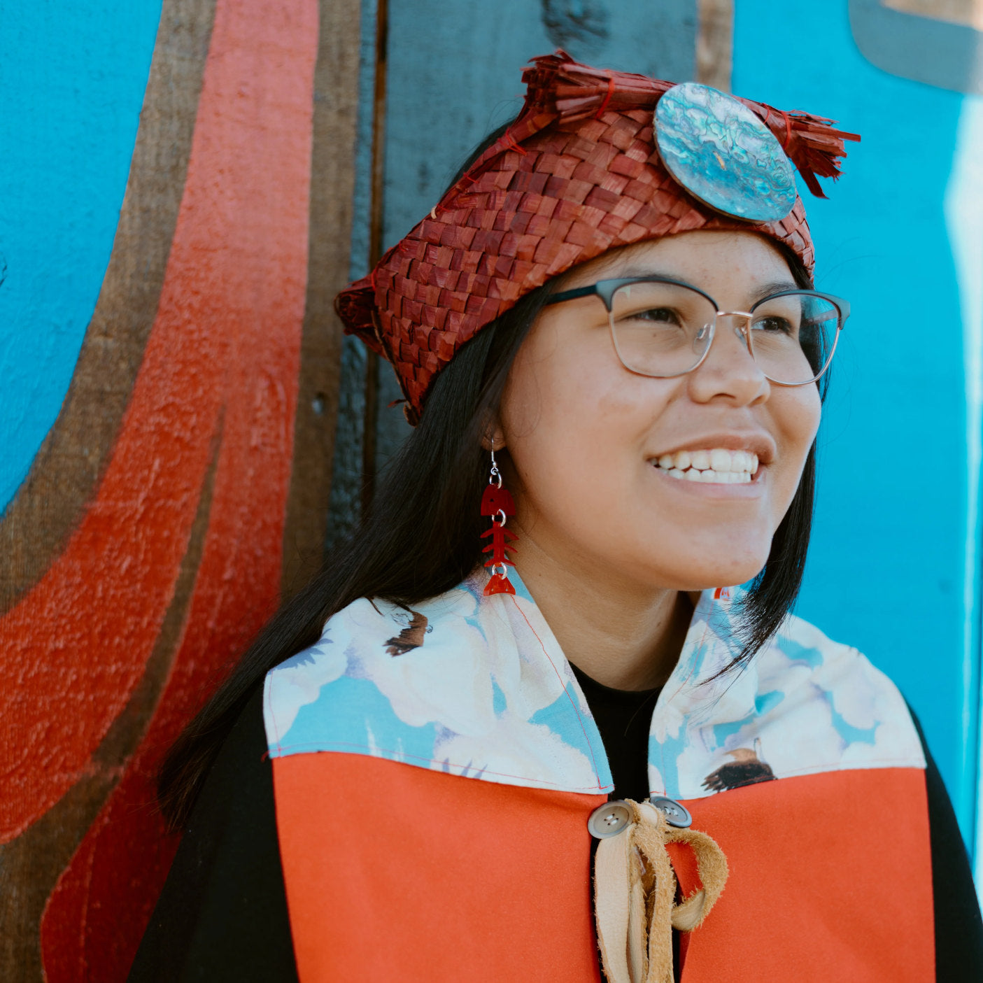 A smiling youth in a cedar headband wearing the red acrylic small salmon ghost earring from Copper Canoe Woman.