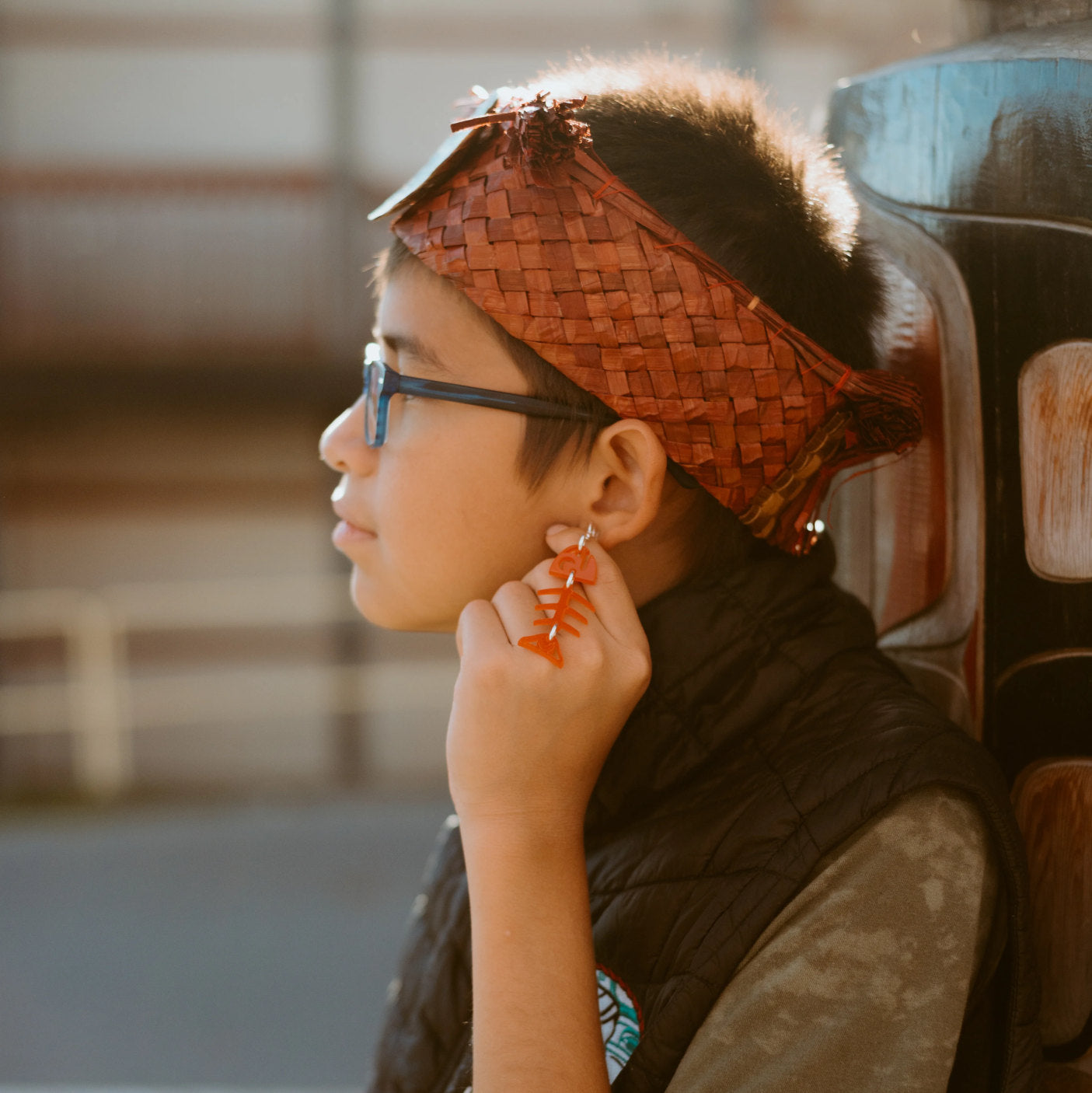 A youth model in profile wearing the red acrylic small salmon ghost earring from Copper Canoe Woman.