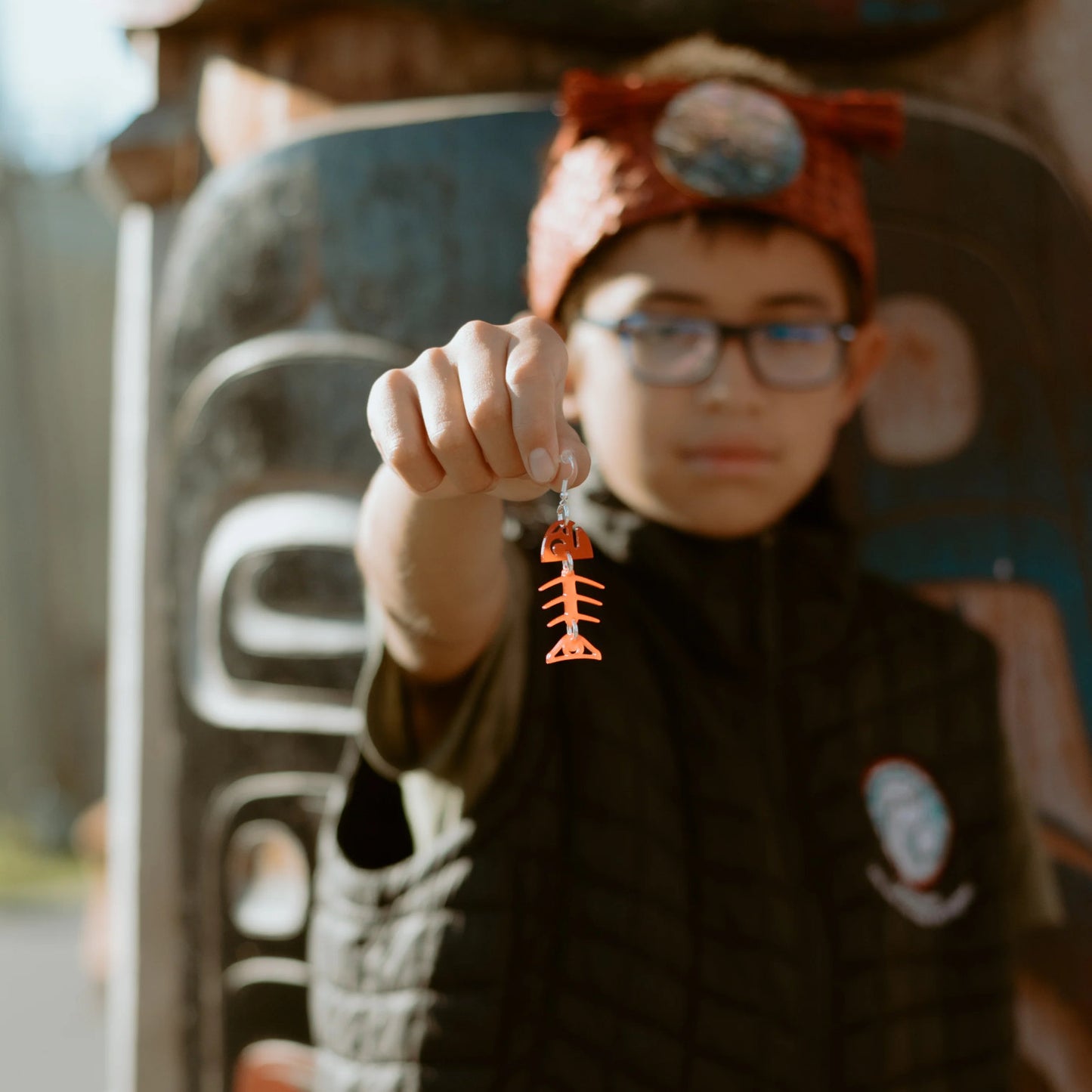 A model holds one Copper Canoe Woman small salmon ghost earring in red acrylic out to the camera.