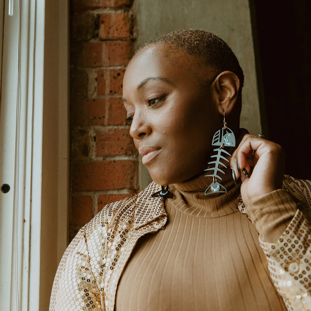 A person looks out a window while wearing black acrylic Medium Salmon Ghost earrings from Copper Canoe Woman.
