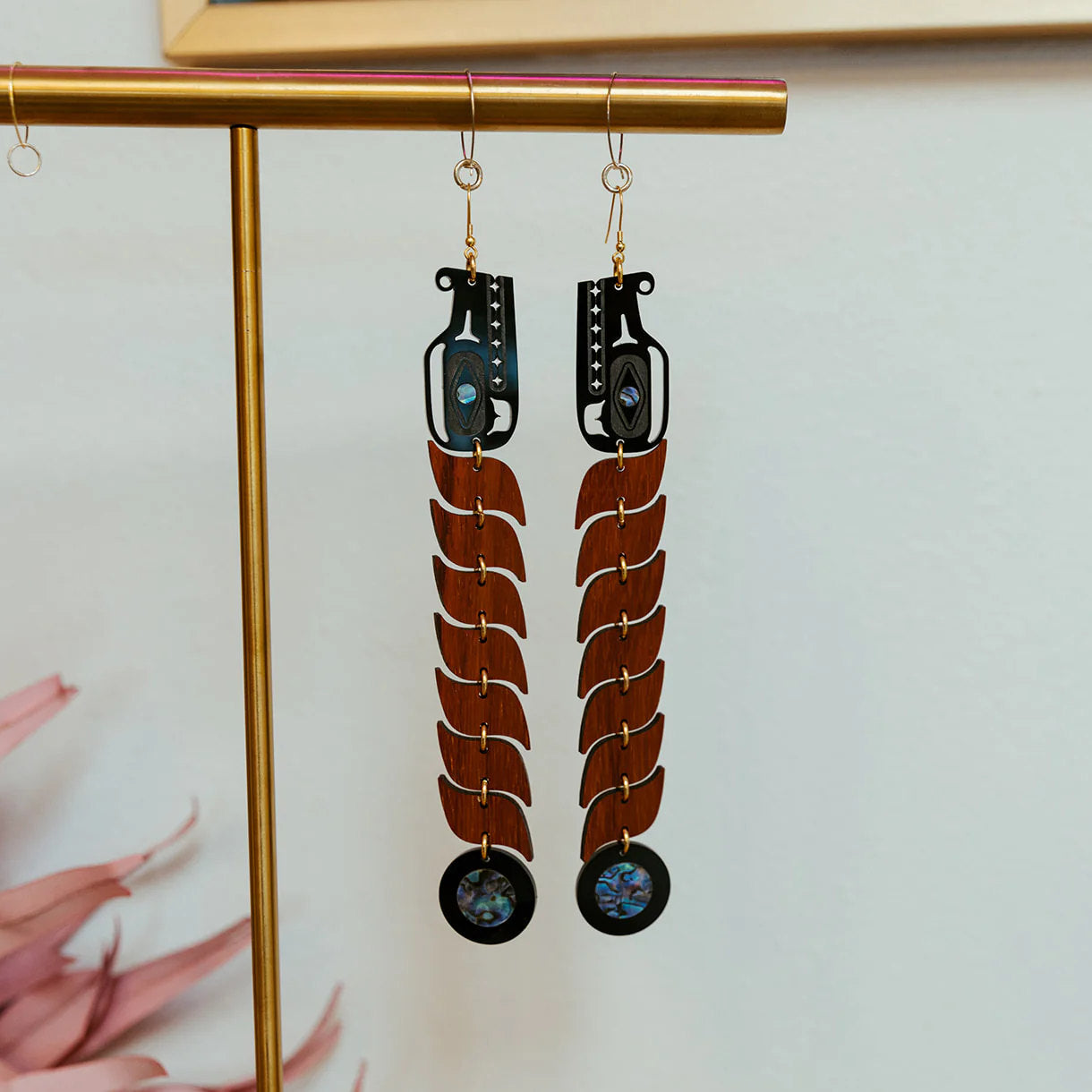 A pair of padauk wood serpent earrings from Copper Canoe Woman hang from a jewelry stand.