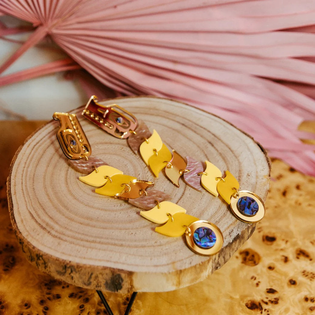 Copper Canoe Woman yellow and gold mirror acrylic serpent earrings laying on a wooden disc.