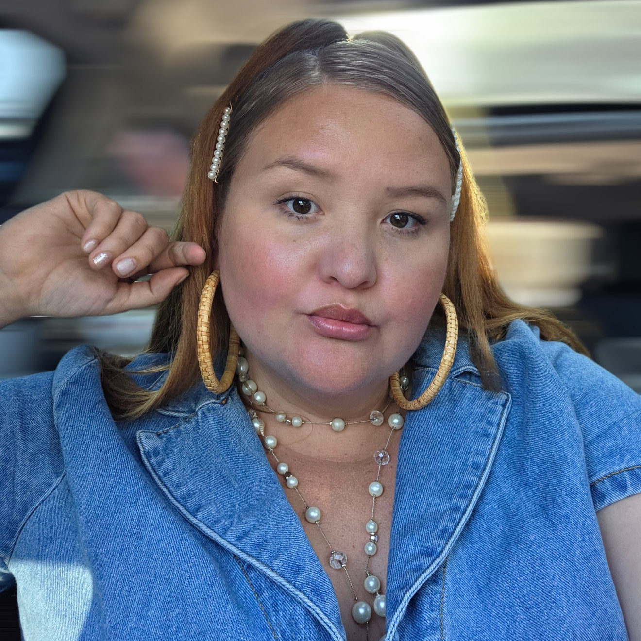 Woman wearing large hoop earrings and a pearl necklace, with a blurred background