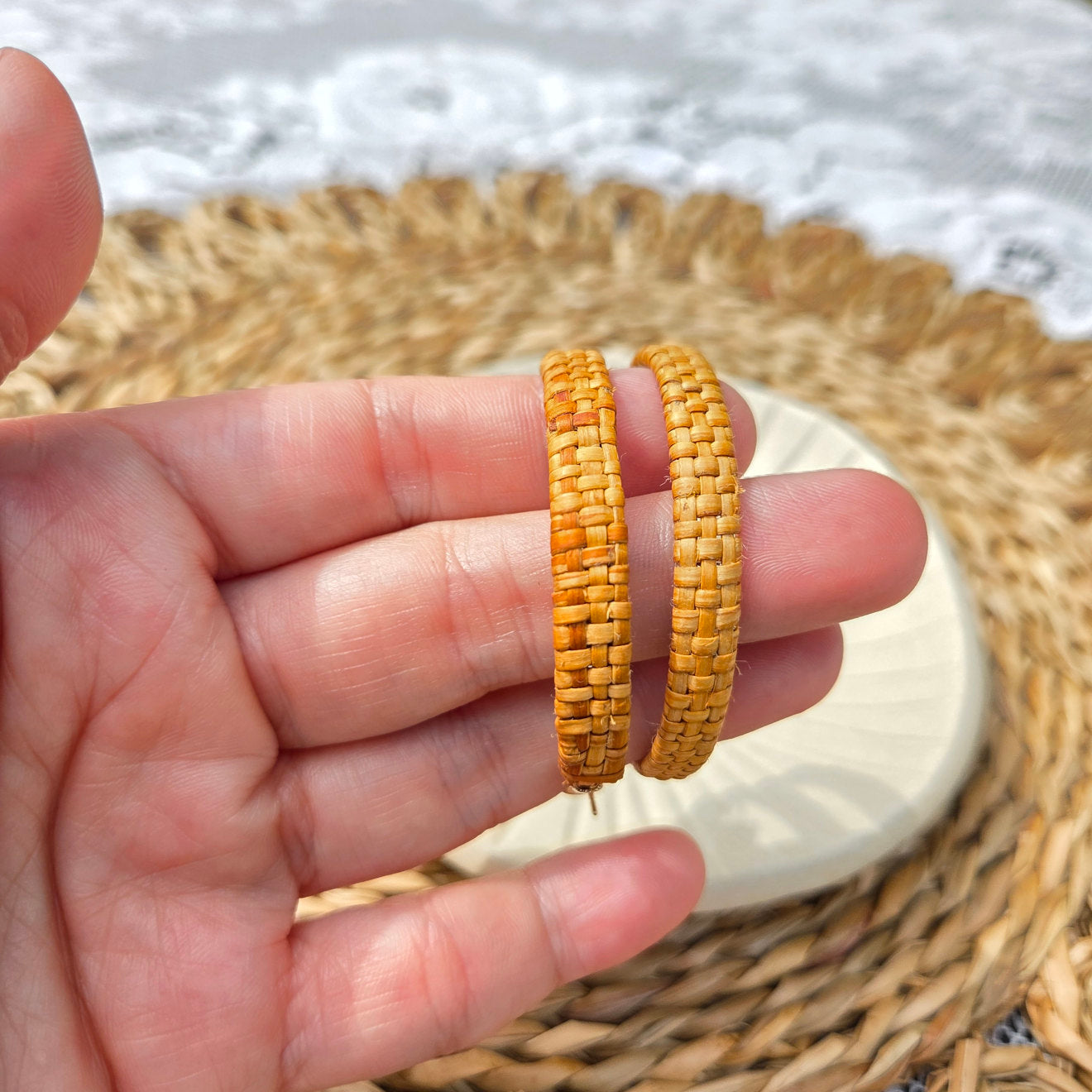 Hand holding two woven bracelets with a blurred natural background