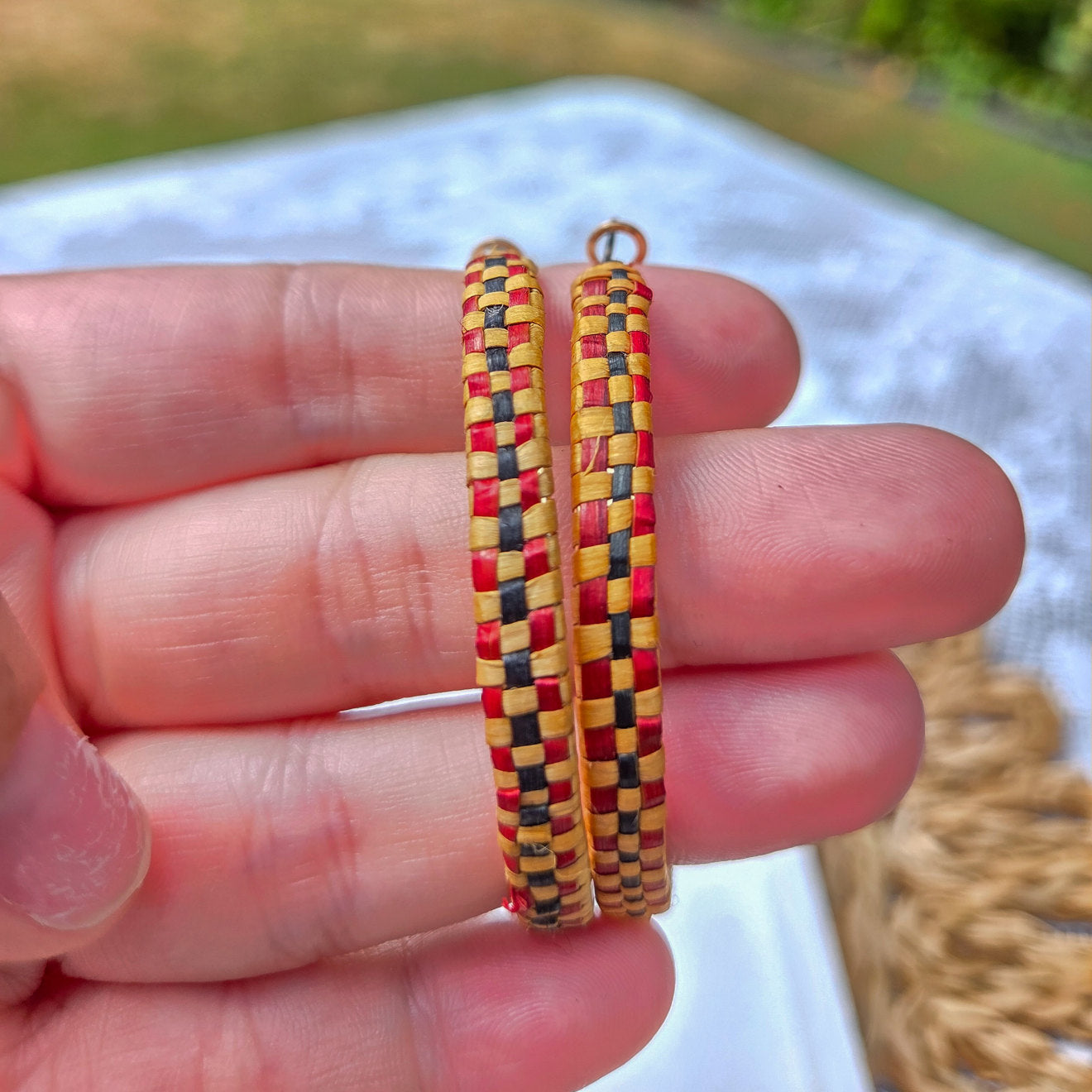 Pair of woven hoop earrings with red and black checkered pattern in hand