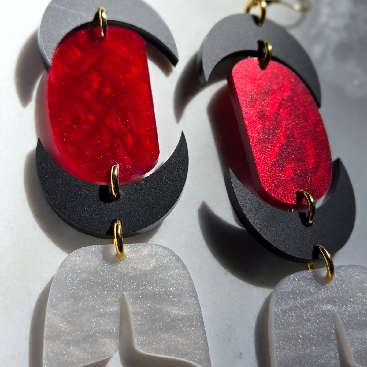Pair of earrings with red and black design on a gray background