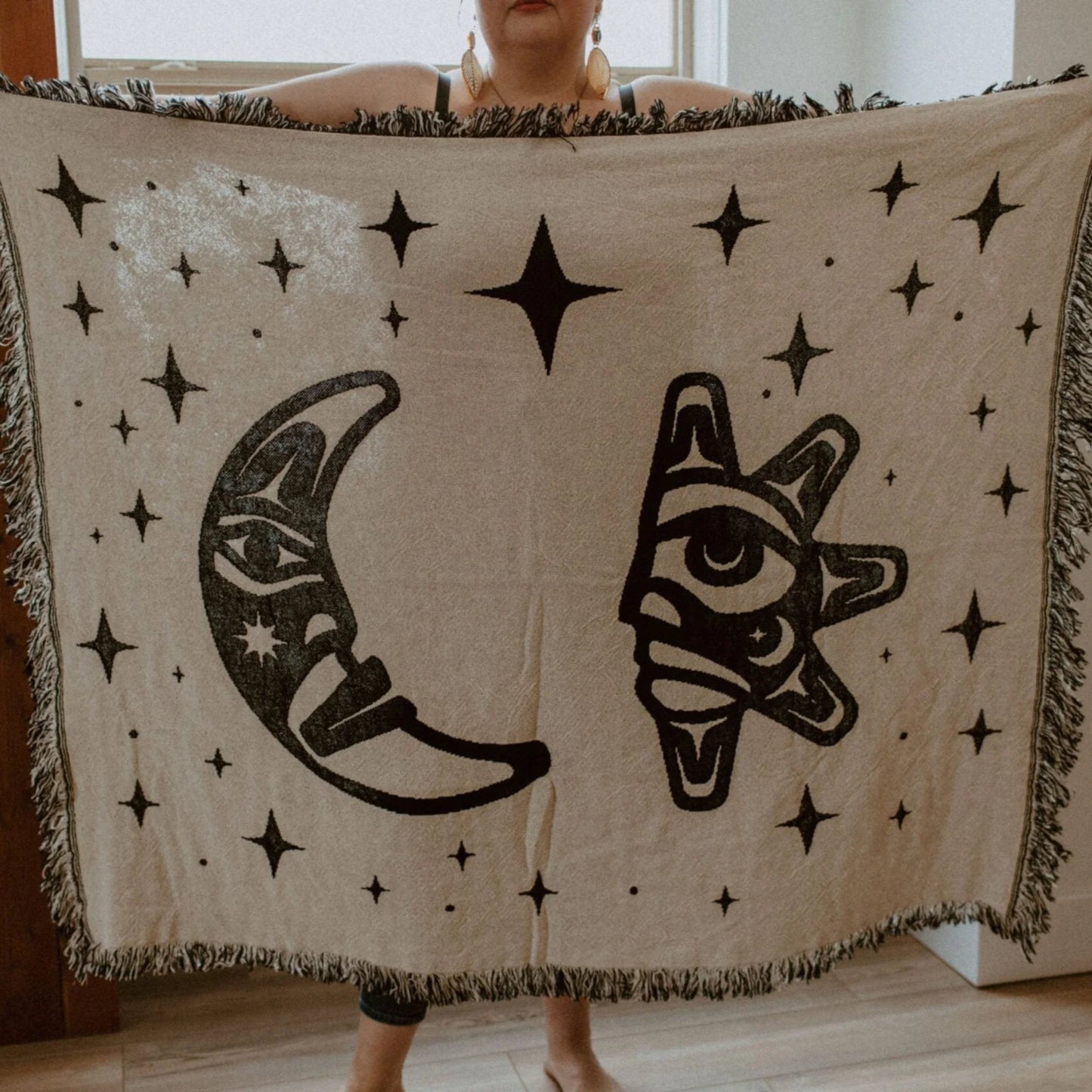 A figure holds open a "Hupal" sun and moon design throw blanket from Copper Canoe Woman.