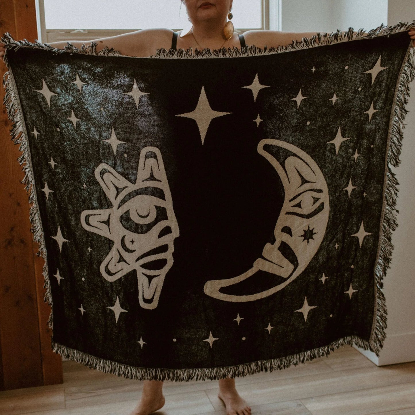A figure holds open the back side of the "Hupal" sun and moon throw blanket from Copper Canoe Woman.