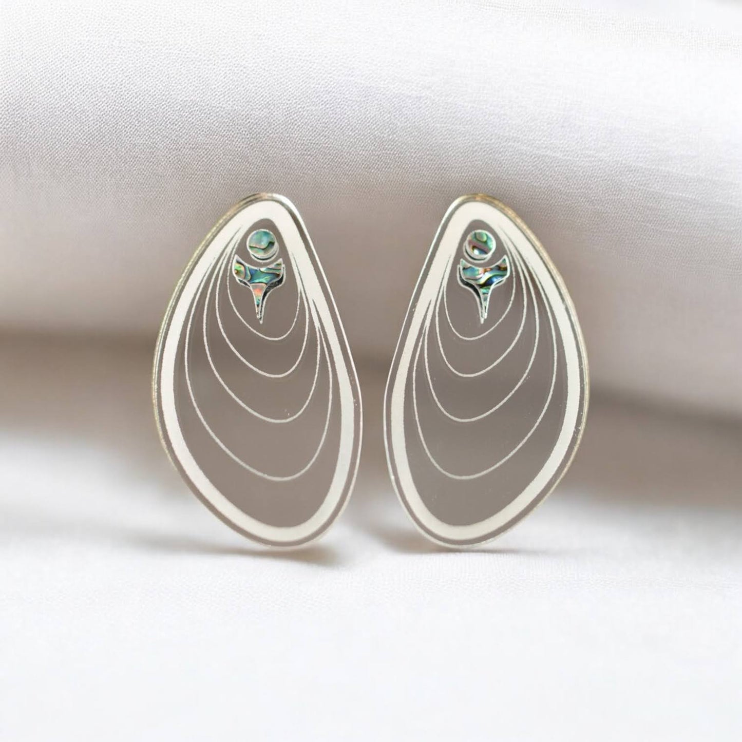 A pair of silver mirror "Tidal Ripples" earrings from Copper Canoe Woman stand against a fold of white fabric.