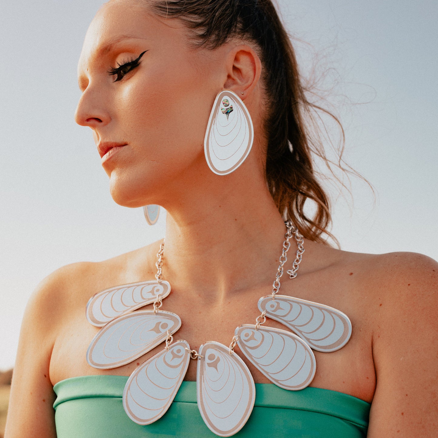 Model wearing the "Tidal Ripples" earring from Copper Canoe Woman in silver mirror acrylic, with matching mussel-inspired necklace.