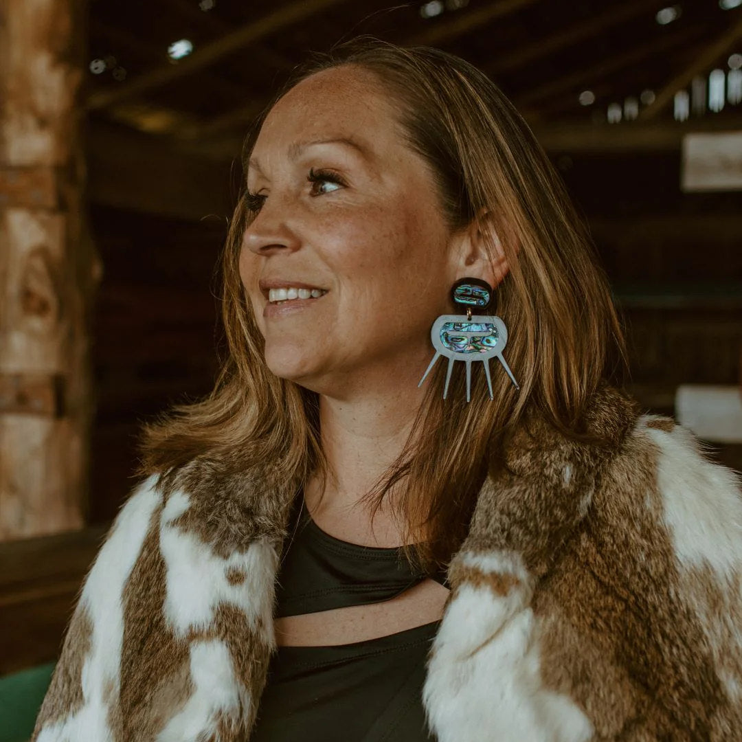 A woman smiles off camera wearing black acrylic Urchin earrings from Copper Canoe Woman