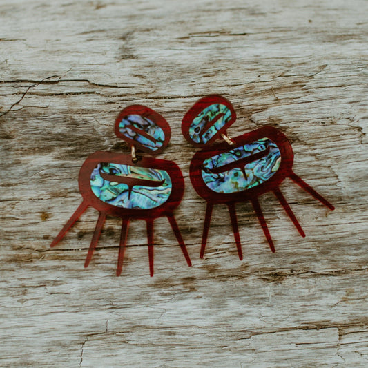 Urchin earrings from Copper Canoe Woman in translucent red acrylic sitting on a log.
