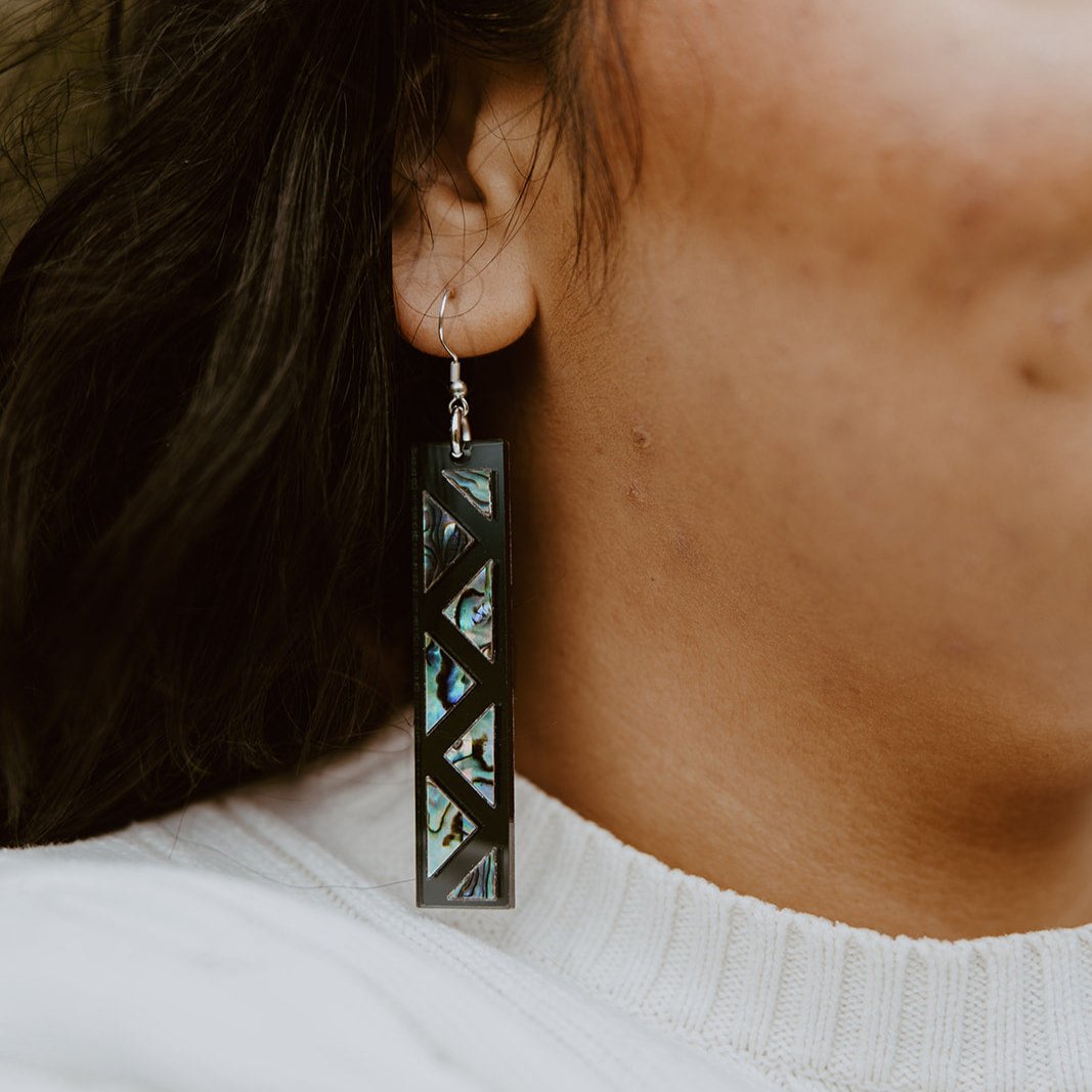 close up of woman wearing charcoal mirror long rectangle warrior spirit earring with triangle zig zag abalone inlay from copper canoe woman