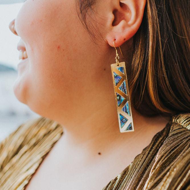 close up of woman wearing gold mirror long rectangle warrior spirit earring with triangle zig zag abalone inlay from copper canoe woman