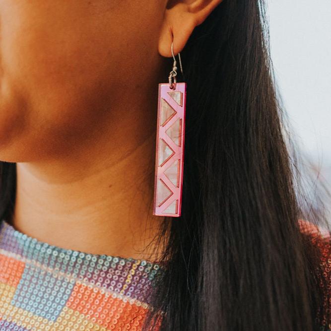 close up of woman wearing pink mirror long rectangle warrior spirit earring with triangle zig zag mother of pearl inlay from copper canoe woman