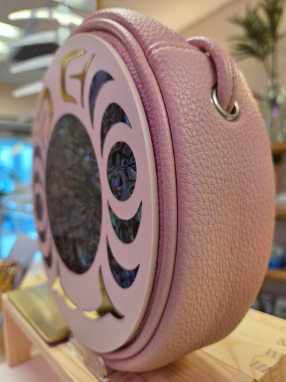 Round pink leather bag with decorative cutouts and abalone shell inlay.