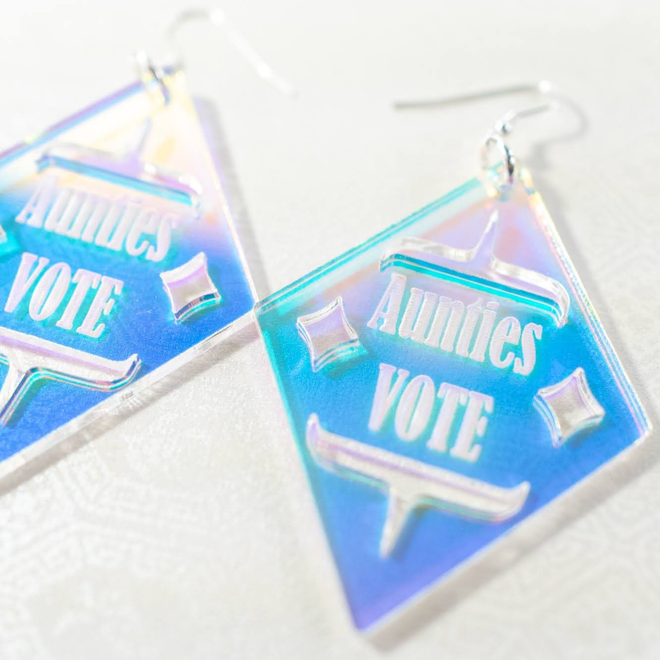 close up of Diamond shaped iridescent earrings with formline cut out and 'Aunties Vote' engraved in the middle from copper canoe woman