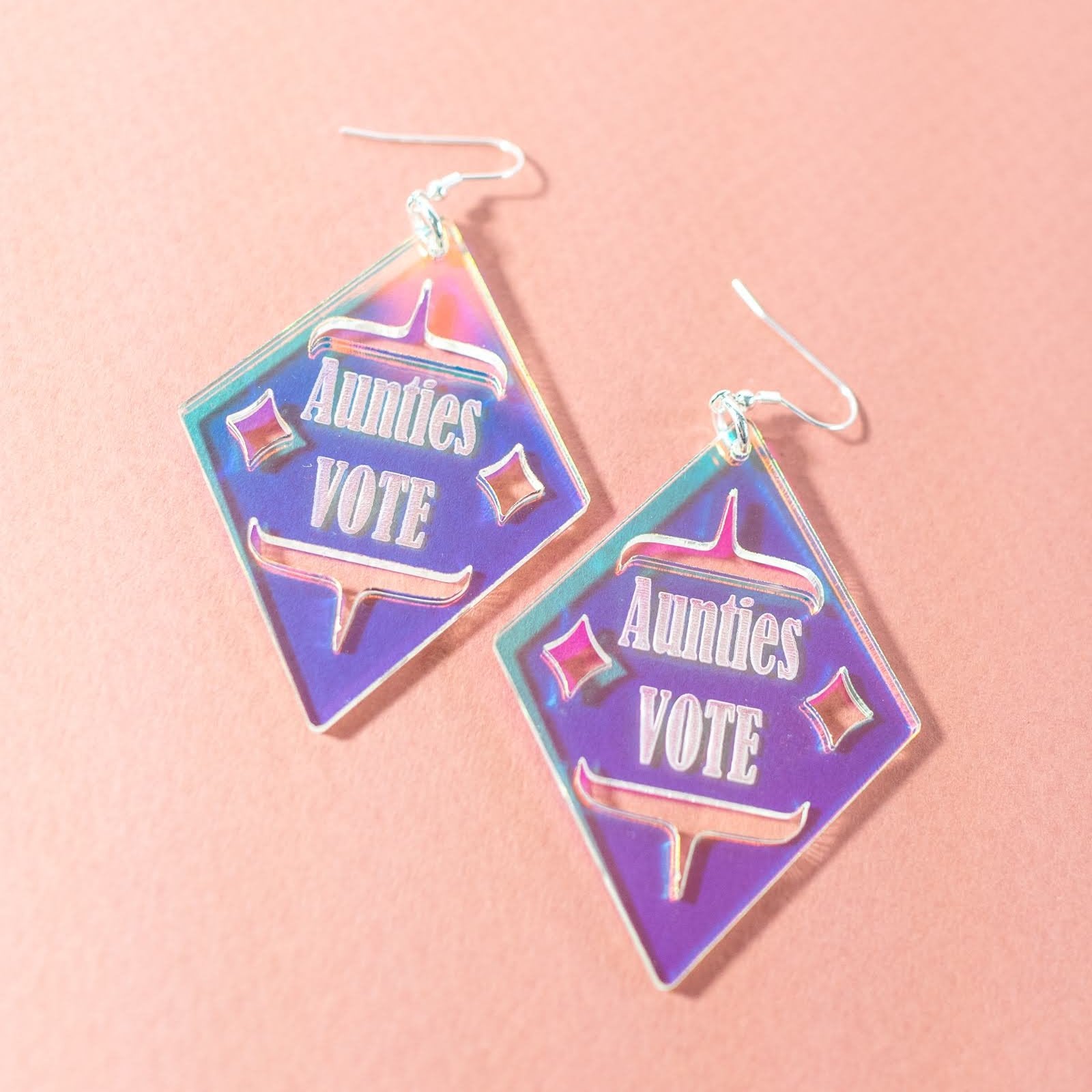 Diamond shaped iridescent earrings with formline cut out and 'Aunties Vote' engraved in the middle from copper canoe woman