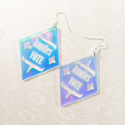 Diamond shaped iridescent earrings with formline cut out and 'Aunties Vote' engraved in the middle from copper canoe woman
