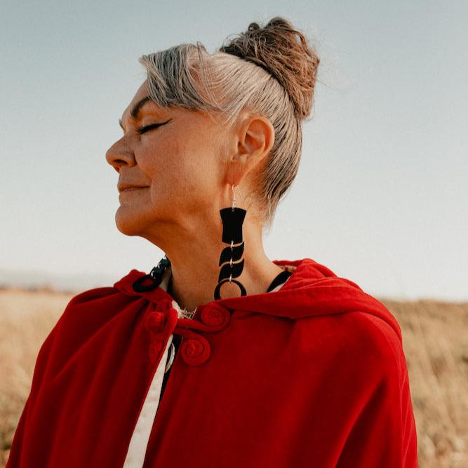 Woman wearing abstract formline art in black color. Top is copper shield, followed by two s shaped formline shapes, and the bottom a circle. earrings from copper canoe woman