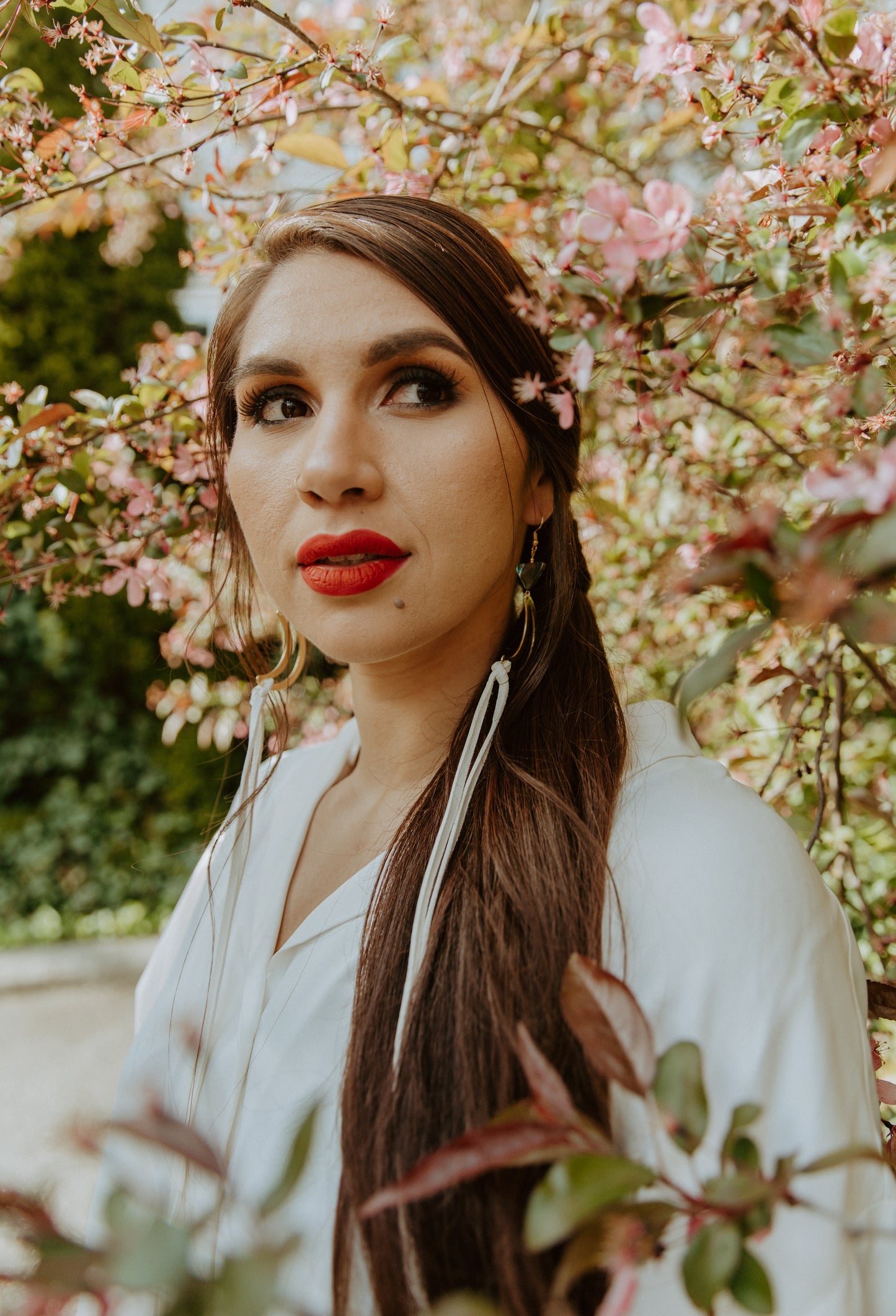 woman wearing Brass crescent moon earrings topped with triangle abalone beads and white fringe hide that hangs from bottom of moon. Designed by Copper Canoe Woman