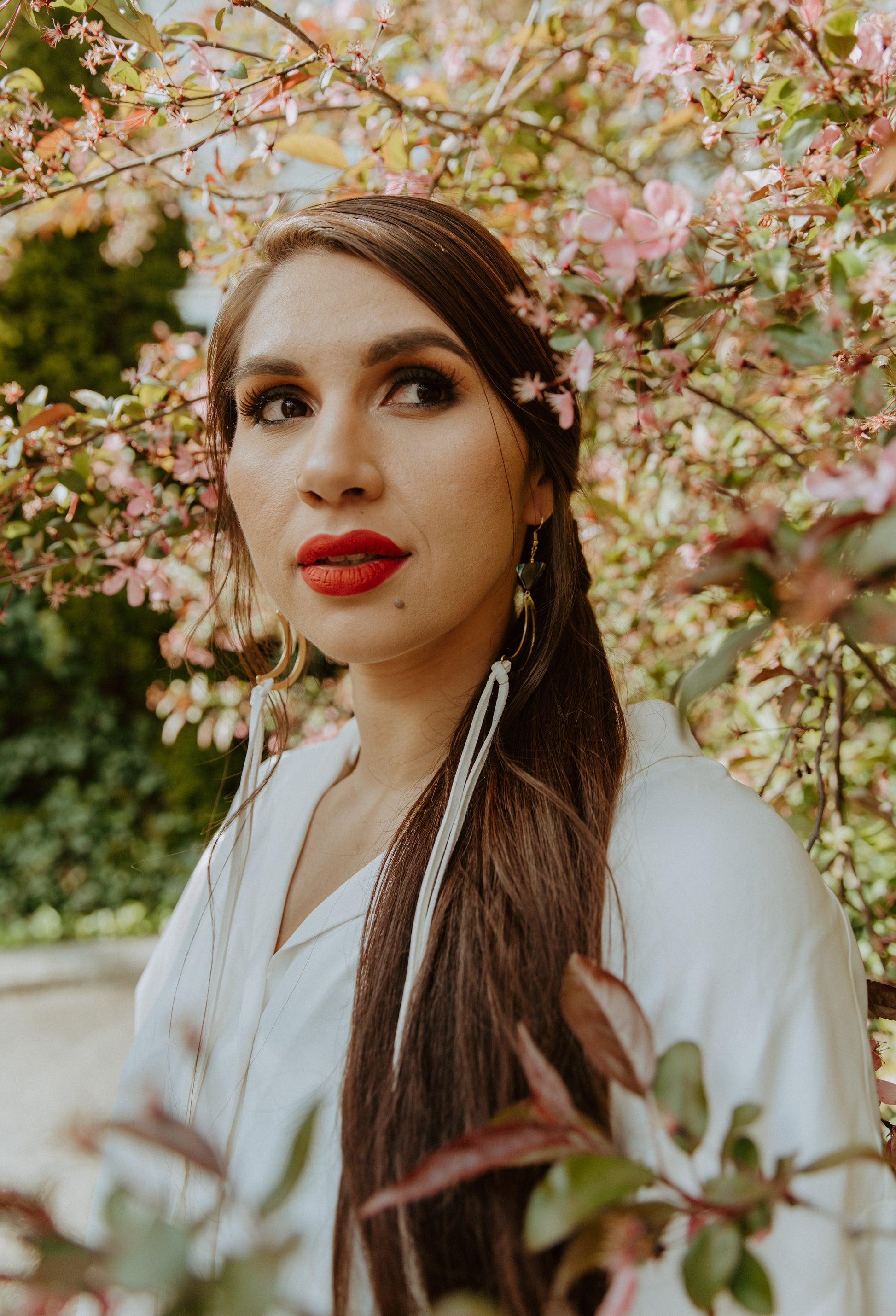 woman wearing Brass crescent moon earrings topped with triangle abalone beads and white fringe hide that hangs from bottom of moon. Designed by Copper Canoe Woman