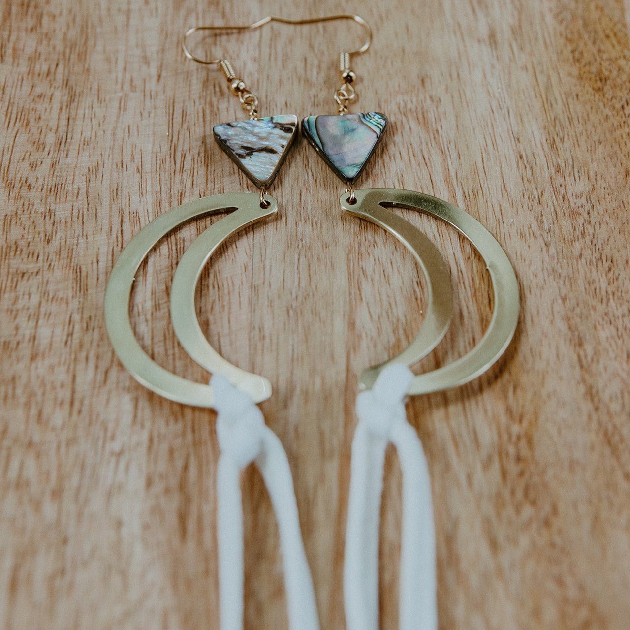 Brass crescent moon earrings topped with triangle abalone beads and white fringe hide that hangs from bottom of moon. Designed by Copper Canoe Woman