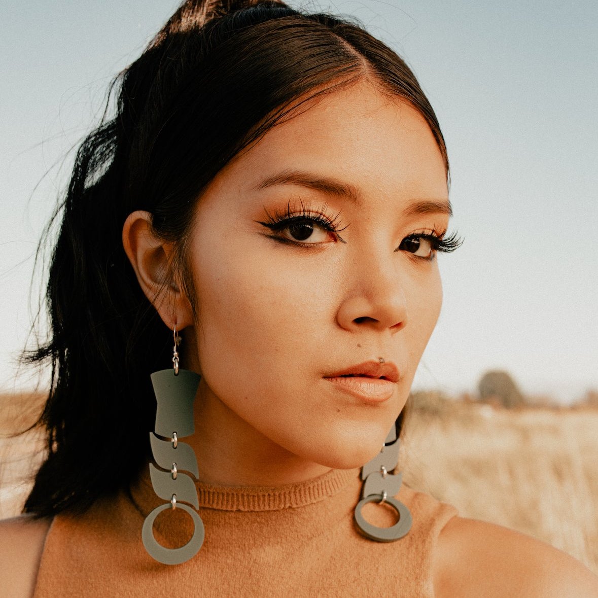 Woman wearing abstract formline art in sage green color. Top is copper shield, followed by two s shaped formline shapes, and the bottom a circle. earrings from copper canoe woman