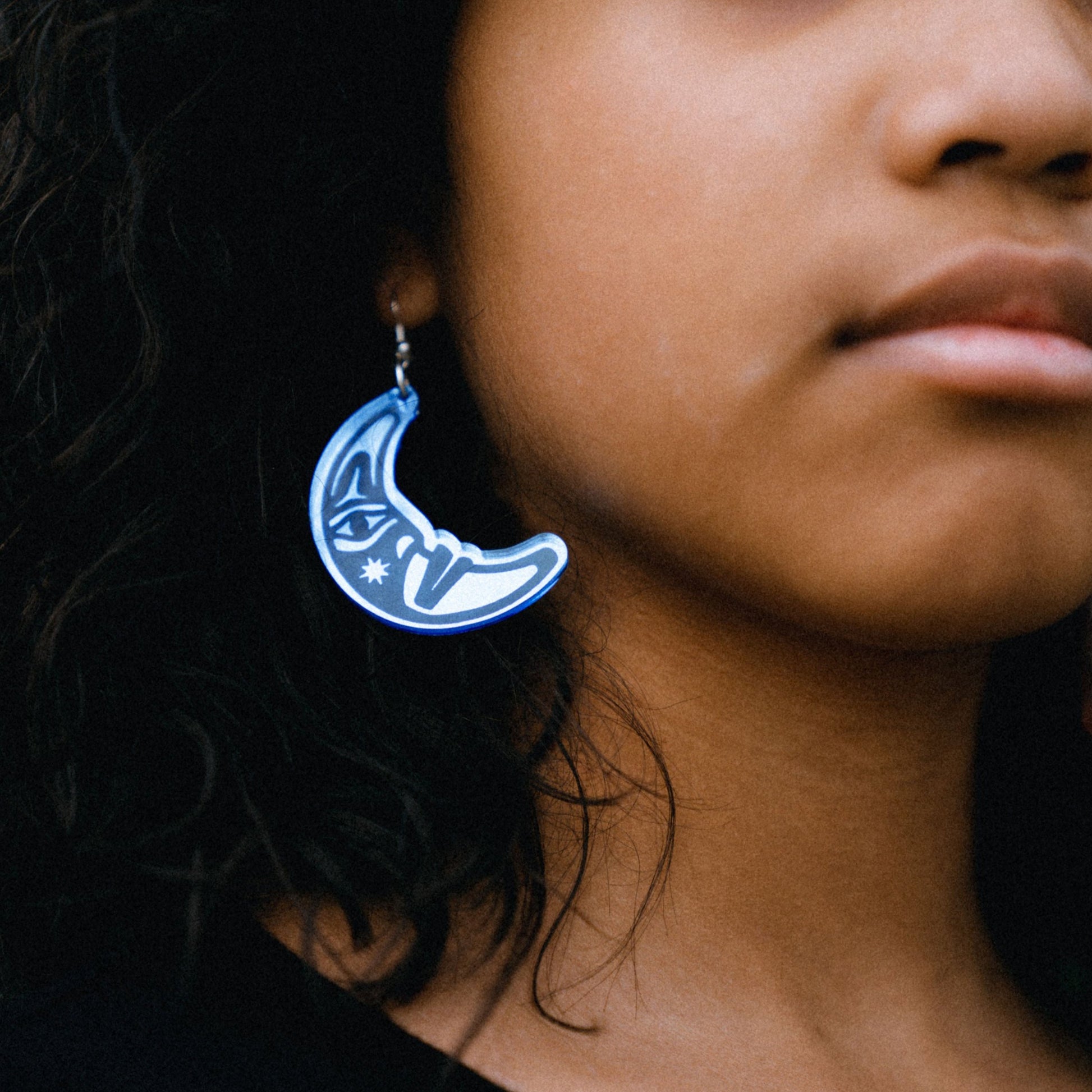 Close up of young woman wearing sky blue acrylic crescent moon engraved with formline art from copper canoe woman
