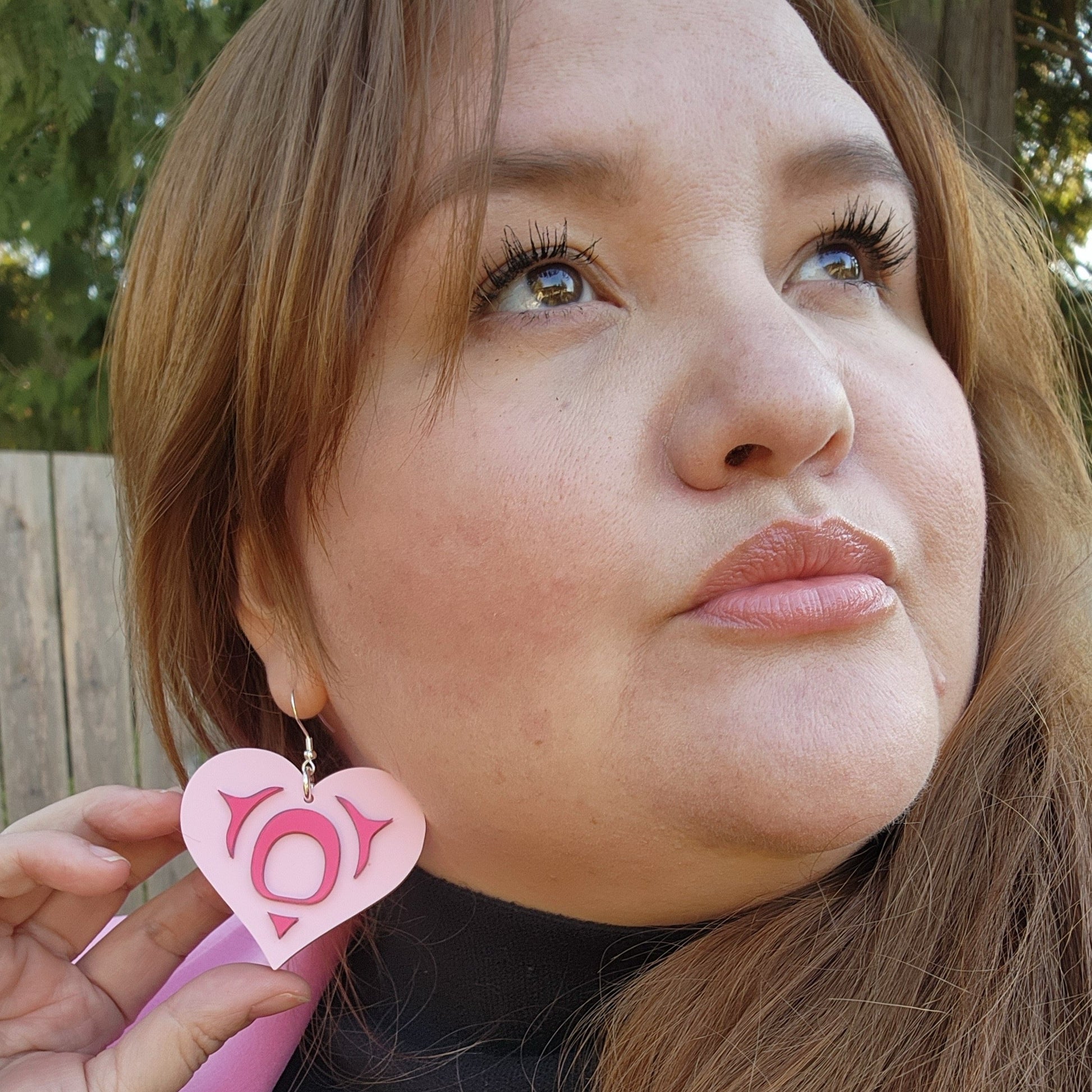 woman looking up to the sky wearing copper canoe woman all my heart earrings in pink acrylic with red acrylic mirror formline art. 