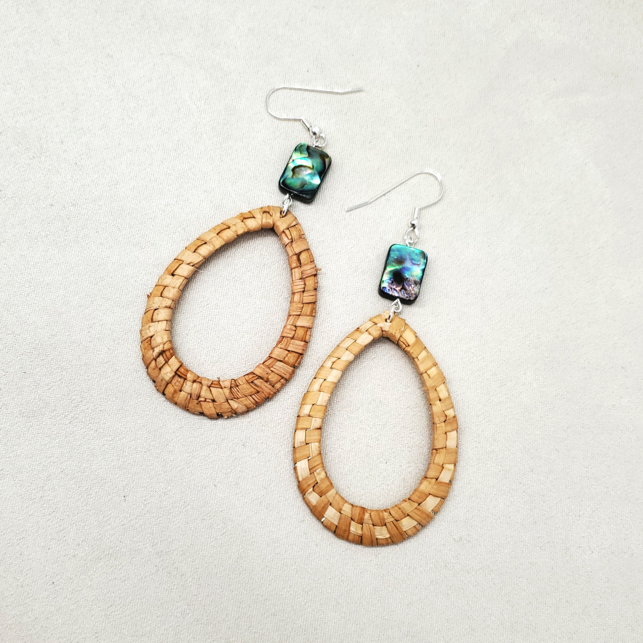 Pair of woven cedar earrings with abalone bead accents on a light gray background