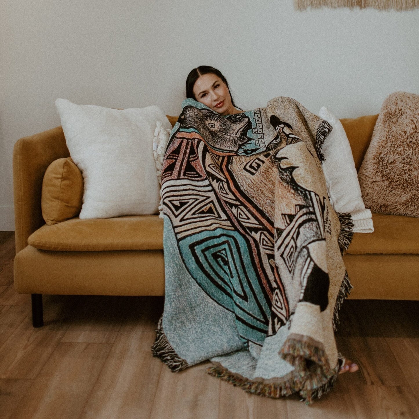 Model wrapped in Hopi bear design throw blanket sits on couch.