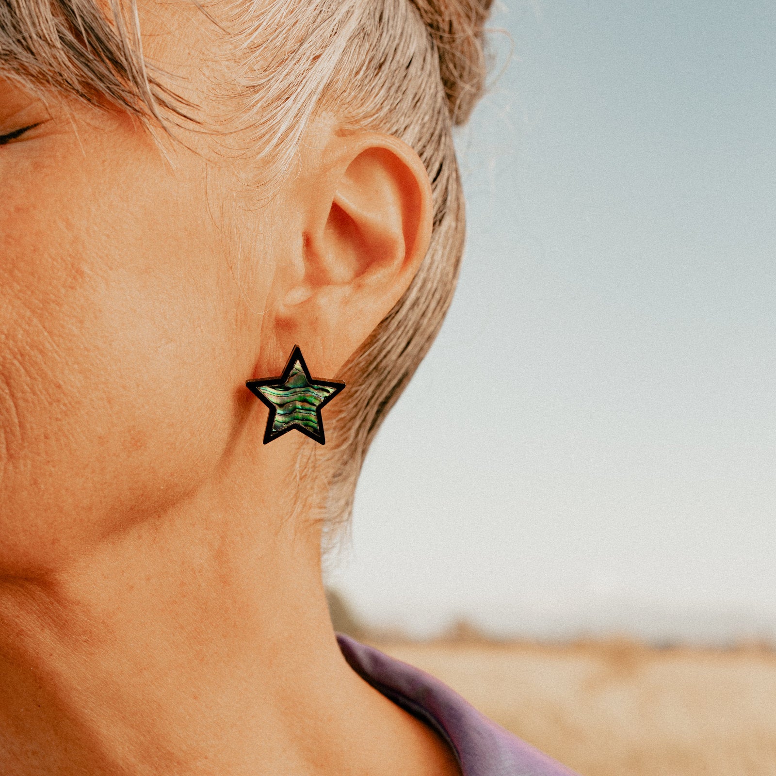 Closeup of model wearing Copper Canoe Woman's "Bright Star" earring in black acrylic and abalone inlay.