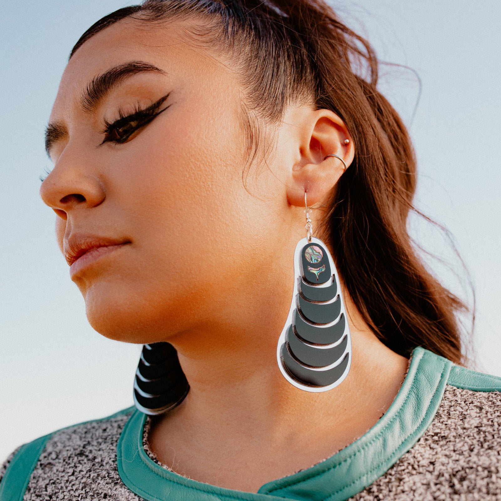 A model in profile wears the "Coastal Strata" earring in black acrylic by Copper Canoe Woman.