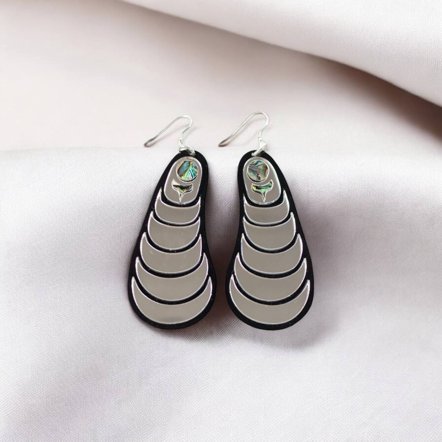 A pair of silver mirror "Coastal Strata" earrings by Copper Canoe Woman laying on white fabric.