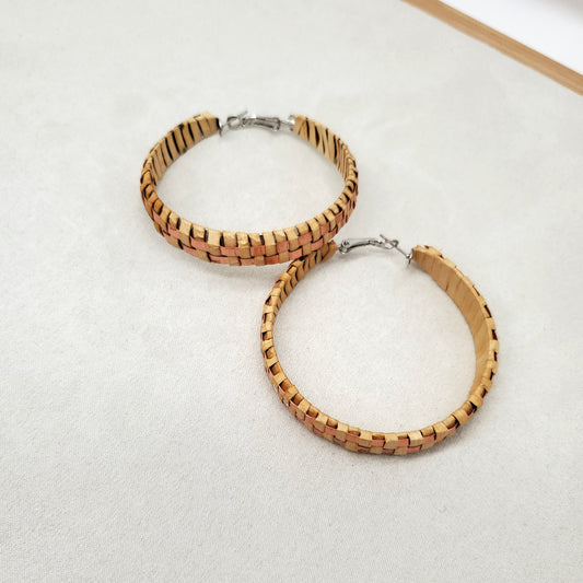 Pair of woven cedar and copper hoop earrings on a light gray background