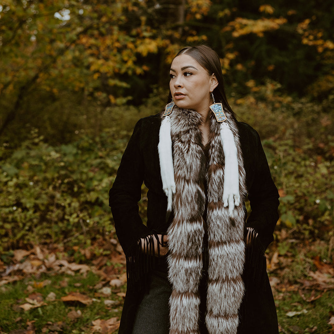 Model stands wearing copper shield shaped cedar earrings with abalone inlay and ermine pelt dangles. Design by Copper Canoe Woman.