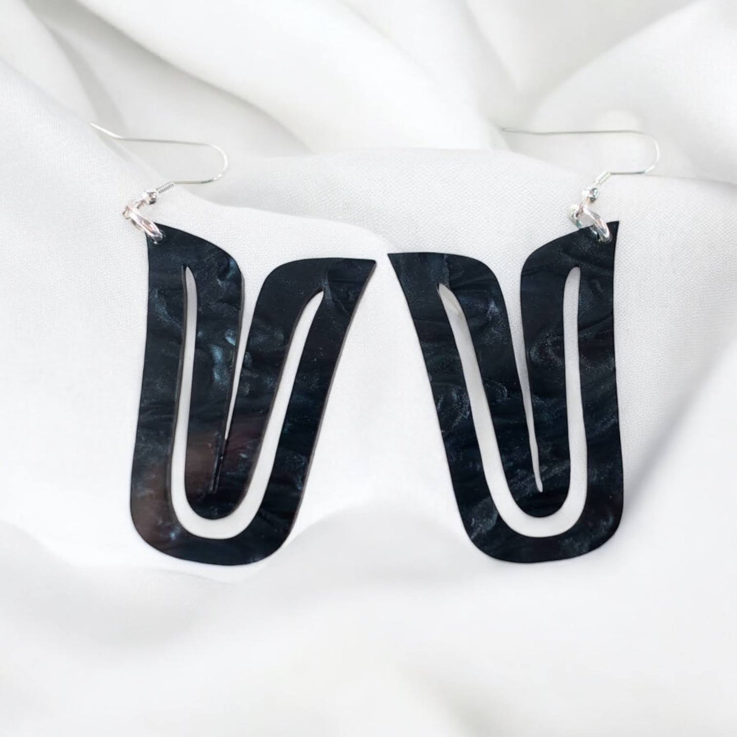 A pair of black acrylic "Echoed U" earrings on white fabric.