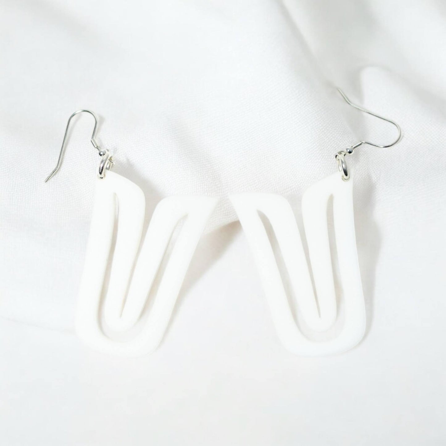 A pair of white acrylic "Echoed U" earrings resting on white fabric.