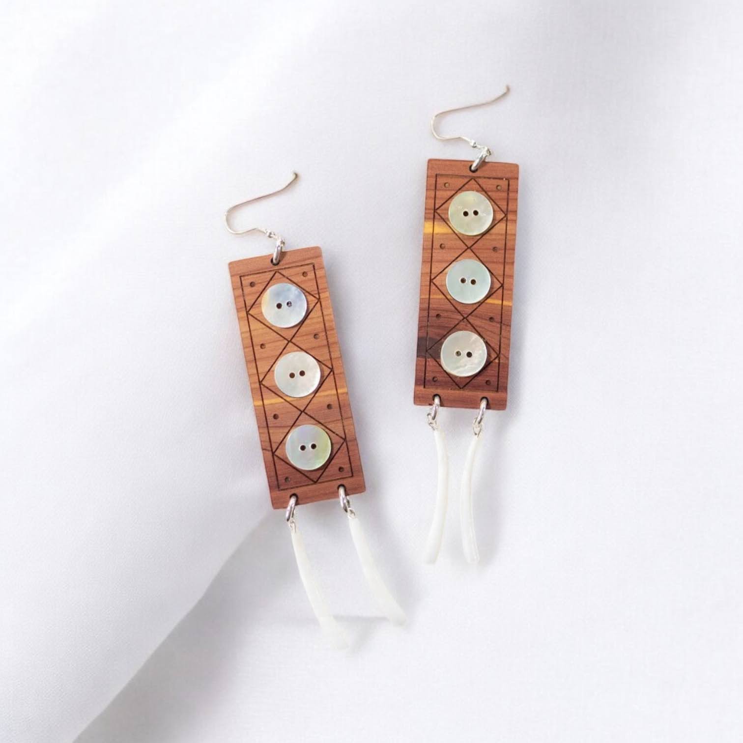 A pair of "Echoes of Celebration" earrings from Copper Canoe Woman  laying on white fabric.