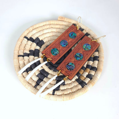 Handmade wooden earrings with abalone inlay and white dentalium shell on woven mat.