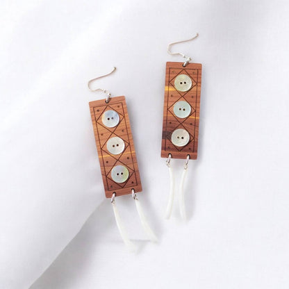A pair of "Echoes of Celebration" earrings from Copper Canoe Woman  laying on white fabric.