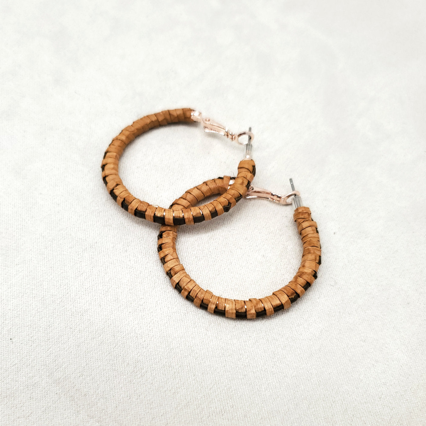 Pair of cedar hoop earrings with black woven details on a light gray background