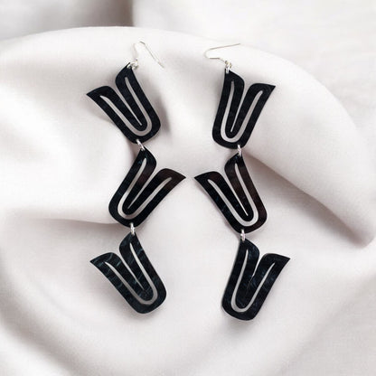 A pair of black "Formline Cascade" earrings from Copper Canoe Woman laying in white fabric.
