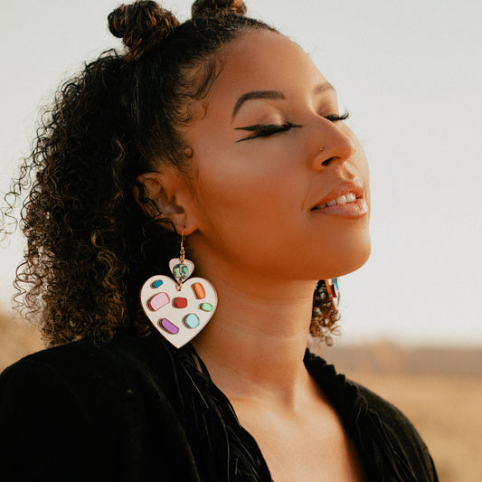 A model enjoys sun on their face in a field while wearing the hook style of the heart-shaped version of the "Generational Love" earring from Copper Canoe Woman.